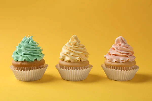 Smakelijke cupcakes met crème op gele achtergrond — Stockfoto