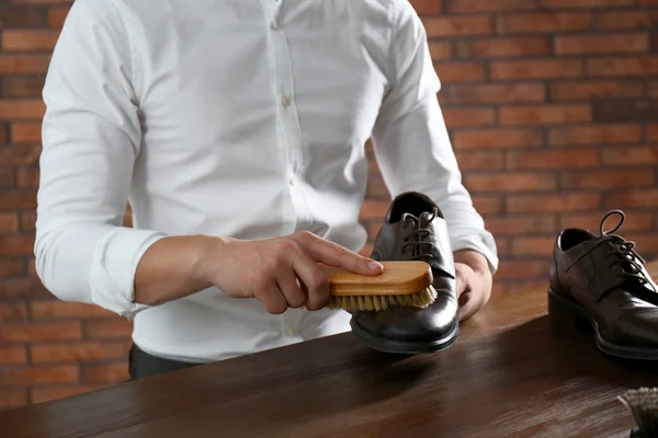 Человек чистки кожаной обуви за деревянным столом в помещении, крупным планом — стоковое фото