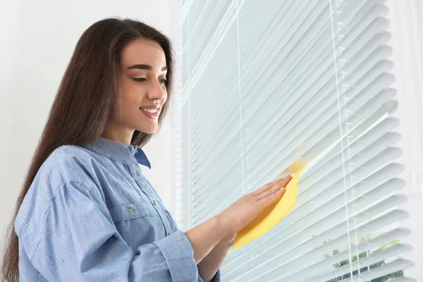 Mooie vrouw schoonmaken raam jaloezieën met Rag binnenshuis — Stockfoto