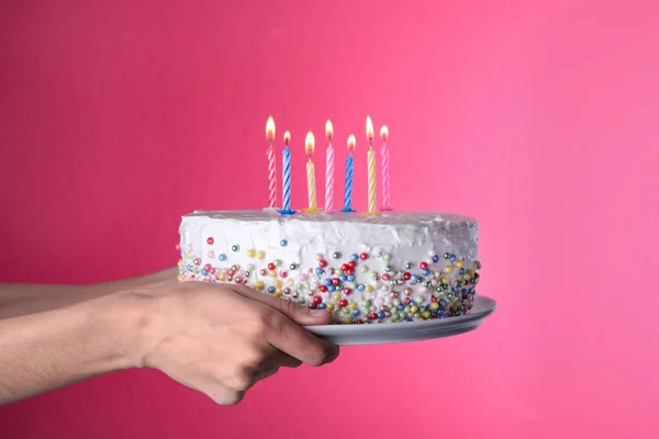 Woman holding birthday cake with burning candles on pink background, closeup — Stock Photo, Image
