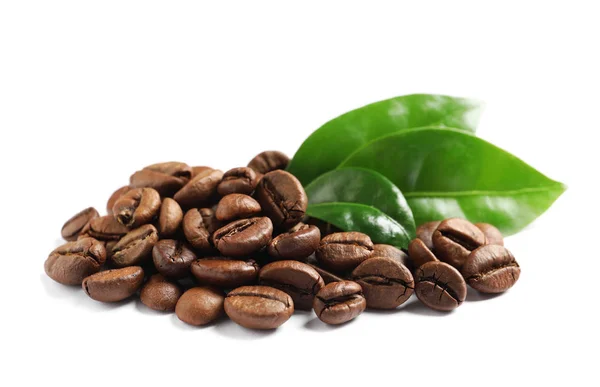 Pražená kávová zrna a čerstvé zelené listy na bílém pozadí — Stock fotografie