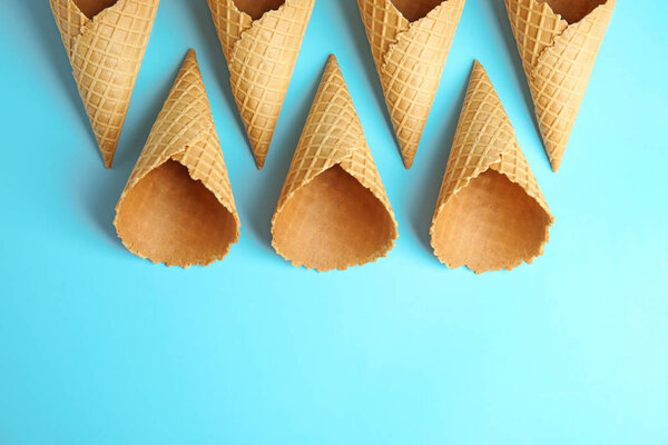 Empty wafer ice cream cones on blue background, flat lay. Space for text