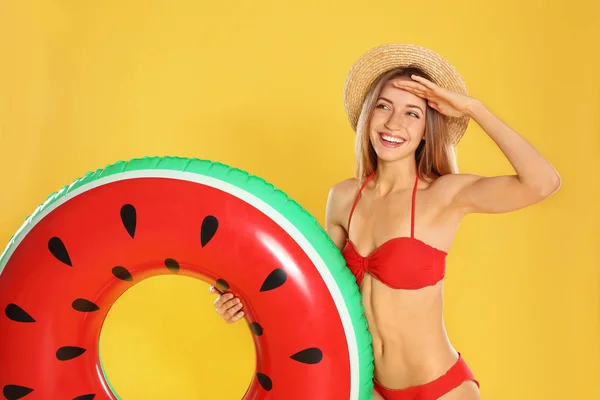 Beautiful young woman in stylish bikini with watermelon inflatable ring on yellow background — Stock Photo, Image