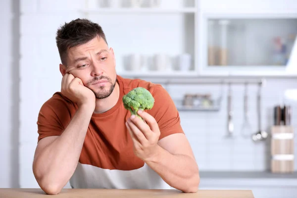 Retrato de homem infeliz com brócolis à mesa na cozinha — Fotografia de Stock