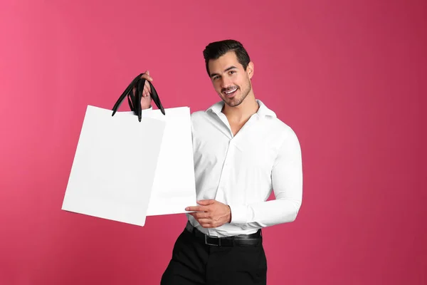 Νέος όμορφος άντρας που κρατά λευκές χάρτινες σακούλες σε ροζ φόντο. Σχέδιο για το σχεδιασμό — Φωτογραφία Αρχείου