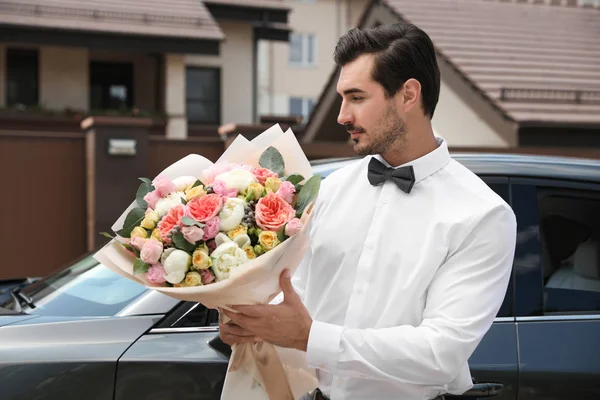 Joven hombre guapo con hermoso ramo de flores cerca de coche al aire libre —  Fotos de Stock