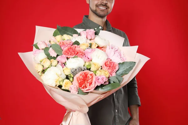 Jovem homem bonito com lindo buquê de flores no fundo vermelho, vista close-up — Fotografia de Stock