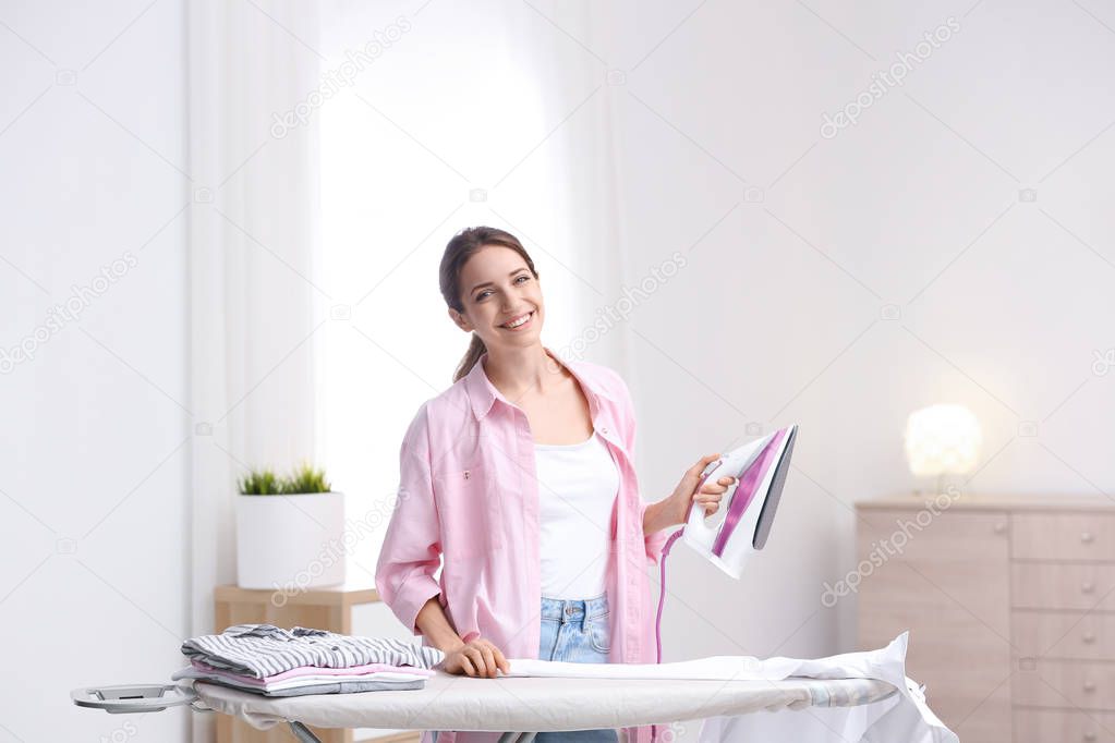Young pretty woman ironing clean laundry indoors