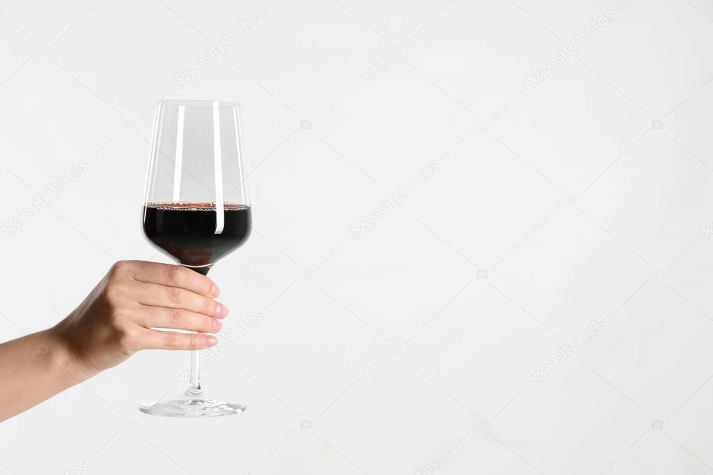 Woman holding glass of red wine on light background, closeup. Space for text