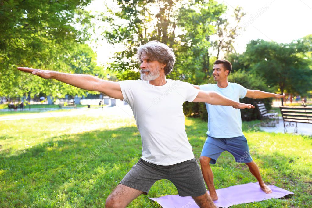 Men practicing morning yoga in sunny park