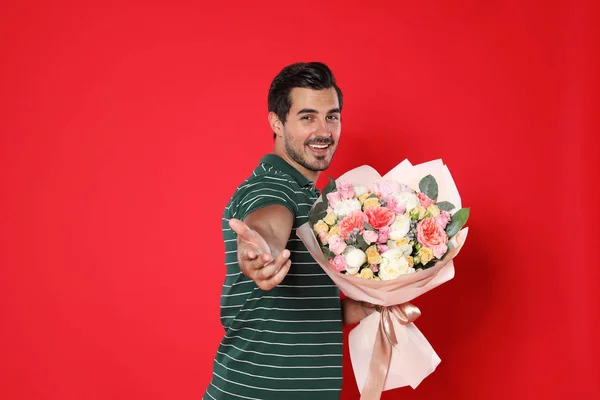 Jovem homem bonito com lindo buquê de flores no fundo vermelho — Fotografia de Stock