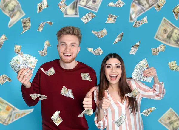 Feliz pareja joven con dólares bajo la lluvia de dinero sobre fondo azul — Foto de Stock