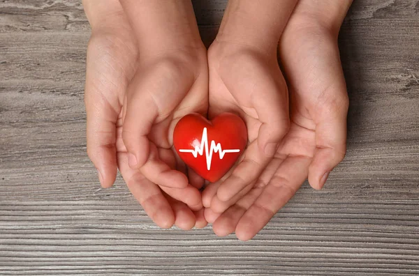 Woman and child holding heart on wooden background, top view. Donation concept — Stock Photo, Image