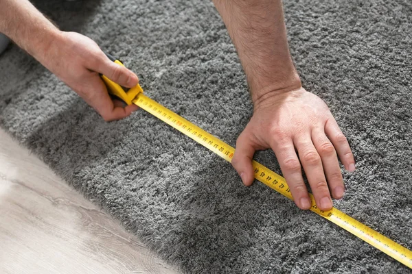 Man measuring grey fluffy carpet indoors, closeup. Construction tool