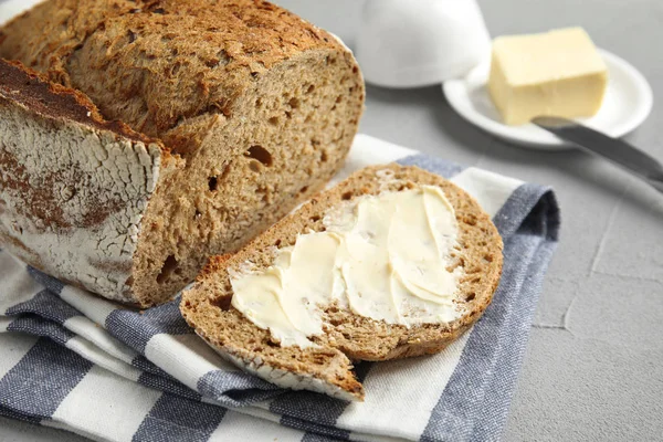 Stukje smakelijk brood met boter in de buurt van Loaf op grijze tafel — Stockfoto