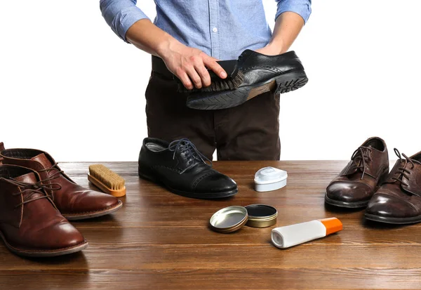Man cleaning leather shoe at wooden table against white background, closeup