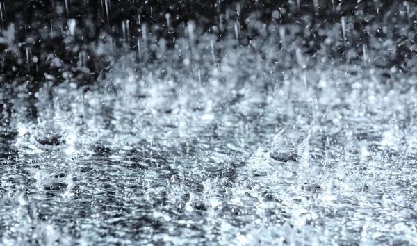 Heavy rain falling down on ground against dark background — Stock Photo, Image