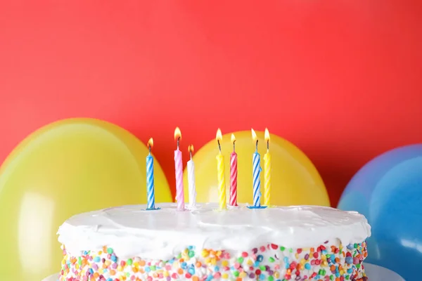 Tasty birthday cake with burning candles and balloons on red background, space for text — Stock Photo, Image