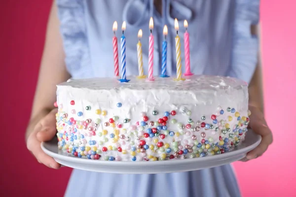 Жінка тримає торт на день народження з палаючими свічками на рожевому фоні, крупним планом — стокове фото