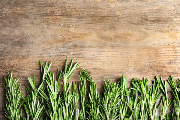 Branches of fresh rosemary on wooden table, top view with space for text