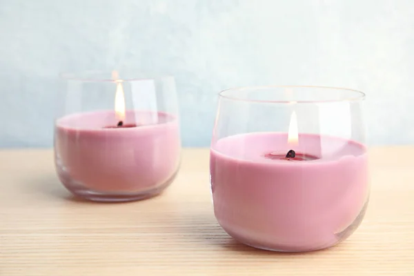 Hořící voskové svíčky ve skleněném skle na dřevěném stole — Stock fotografie