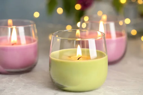 Горящие свечи в стеклянных держателях на сером столе против размытых огней — стоковое фото