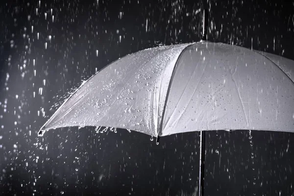 Paraguas blanco bajo la lluvia sobre fondo oscuro — Foto de Stock