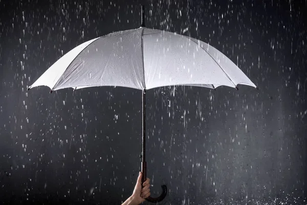 Mulher segurando guarda-chuva branco sob chuva no fundo escuro, close-up — Fotografia de Stock