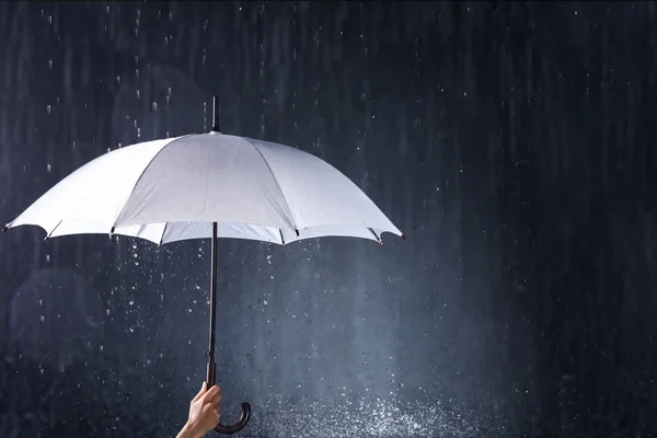 Mulher segurando guarda-chuva branco sob chuva no fundo escuro, close-up — Fotografia de Stock