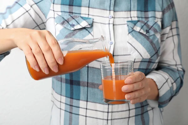 Woman pouring tasty carrot juice from bottle into glass on grey background, closeup — Stock Photo, Image