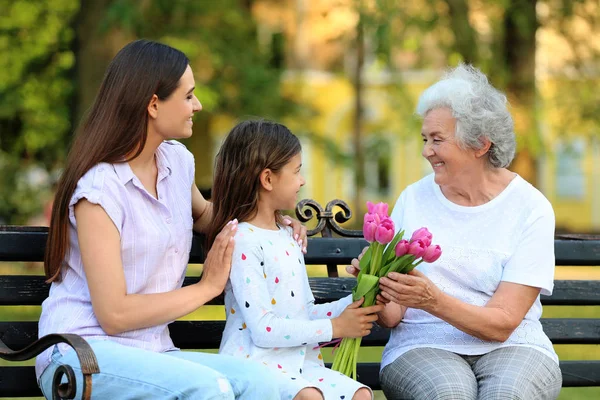 Großmutter erhält Blumenstrauß von ihrer Familie auf Parkbank — Stockfoto