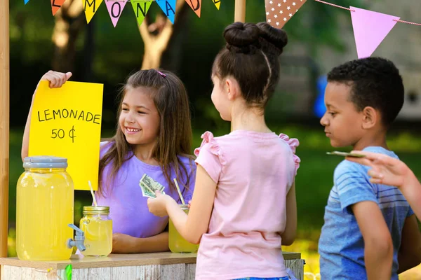 Liten flicka som säljer naturlig lemonad till barn i parken. Sommar uppfriskande drink — Stockfoto