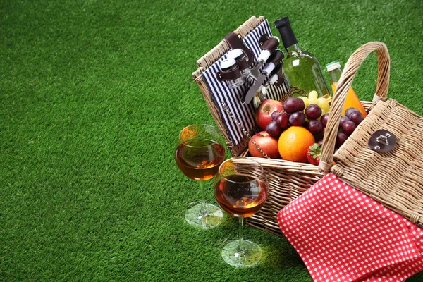 Плетеная корзина для пикника с различными продуктами на зеленой траве, место для текста — стоковое фото
