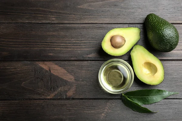 Kom van natuurlijke olie en avocado's op houten achtergrond, platte lag. Ruimte voor tekst — Stockfoto
