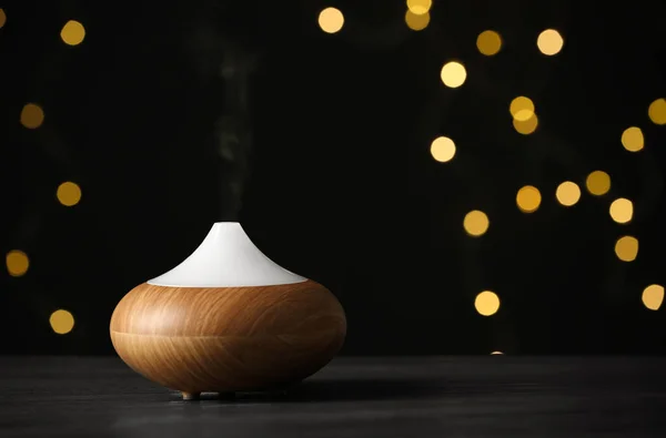 Moderní esenciový difuzní olej na dřevěném stole proti rozmazané světlech, prostor pro text — Stock fotografie