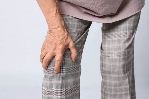 Ηλικιωμένη γυναίκα που έχει προβλήματα στο γόνατο σε γκρίζο φόντο, κοντινό πλάνο — Φωτογραφία Αρχείου