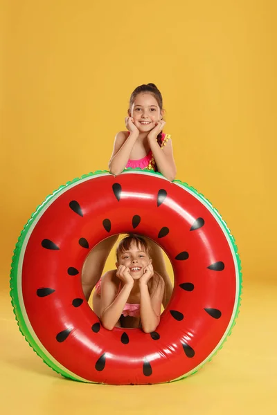 Söta små flickor med ljusa uppblåsbara ring på gul bakgrund — Stockfoto