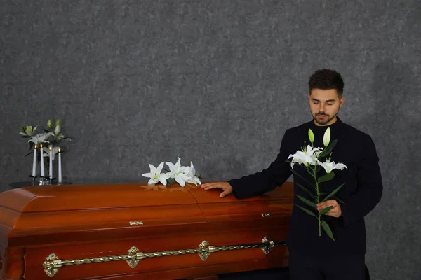 Joven triste con lirios blancos cerca del ataúd en la funeraria — Foto de Stock