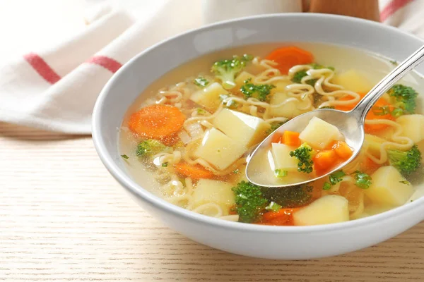 Sendok sup sayuran segar buatan sendiri di atas mangkuk penuh di atas meja kayu, closeup — Stok Foto