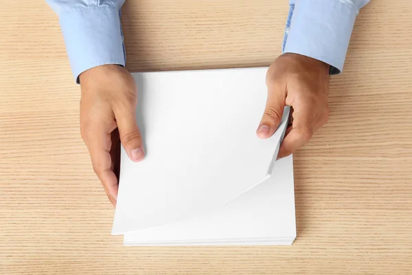 Człowiek trzyma puste arkusze papieru do broszury na drewnianym stole, widok z góry. Makiety — Zdjęcie stockowe