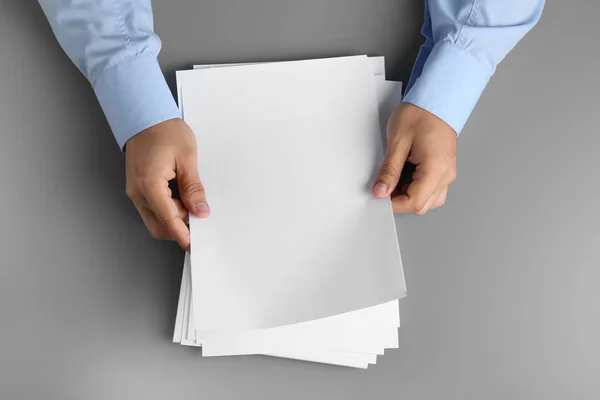 Muž, který drží prázdné papírové listy pro brožuru v šedé tabulce, pohled shora. S předstíranou — Stock fotografie