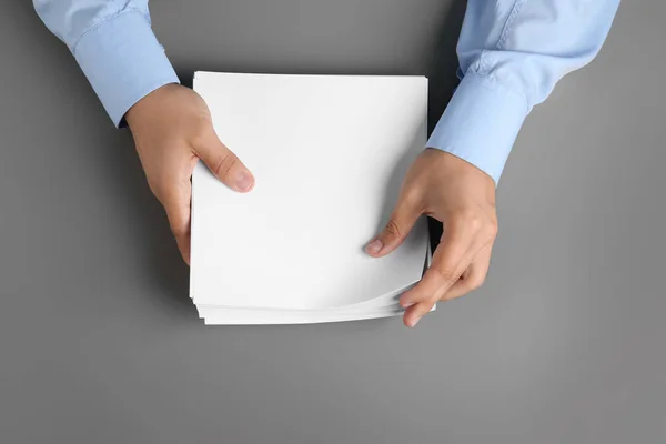 Homem segurando folhas de papel em branco para brochura na mesa cinza, vista superior. Faz asneira. — Fotografia de Stock