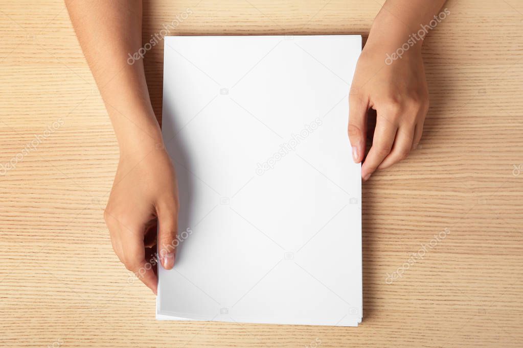 Woman holding blank paper sheets for brochure at wooden table, top view. Mock up