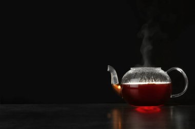 Koyu arka plana karşı masada lezzetli sıcak içecek ile cam çaydanlık. Metin alanı