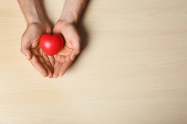 Hafif ahşap arka planda kırmızı kalp tutan genç adam, metin alanı ile üst görünüm. Bağış konsepti