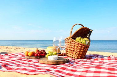 Güneşli plajda piknik sepeti ve ürünleri ile damalı battaniye