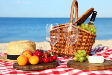 Güneşli plajda piknik sepeti ve ürünleri ile damalı battaniye