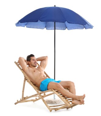 Beyaz arka plana karşı şemsiye altında şezlonsun üzerinde genç adam. Plaj aksesuarları