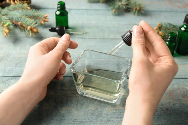 Mujer goteando aceite esencial en un tazón con pipeta en la mesa de madera, primer plano — Foto de Stock