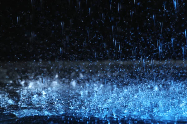 Lluvia fuerte cayendo sobre el suelo sobre fondo oscuro, tonificado en azul — Foto de Stock